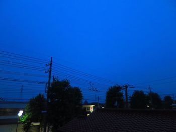 Silhouette trees and electricity pylon against clear blue sky