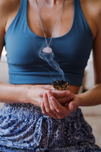 Woman sitting on the carpet meditating and burning sage wearing crystal necklace