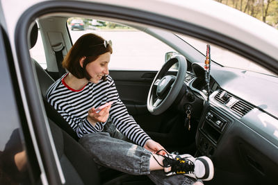 Portrait of a young brunette woman driving in a car using a smartphone