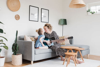 Mother and daughter sat playing guitar together laughing at home