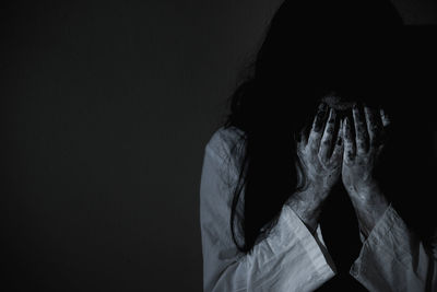 Midsection of person covering face against black background