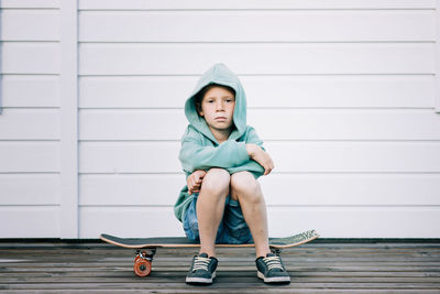 Young boy sat on a skateboard with a hoodie on looking grumpy