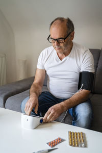 Man measuring blood pressure through device sitting on sofa at home