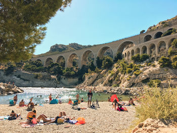 People at beach against old ruins in sunny day