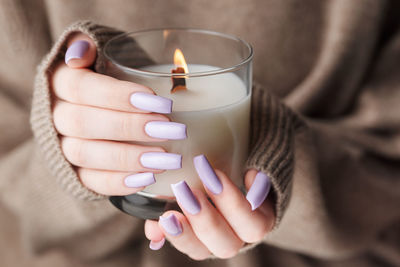 The hands of a young girl with a beautiful light purple manicure hold a candle. 