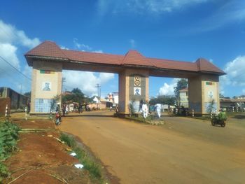 People walking on road by buildings against blue sky