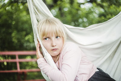 Thoughtful girl looking away while sitting on white swing in garden