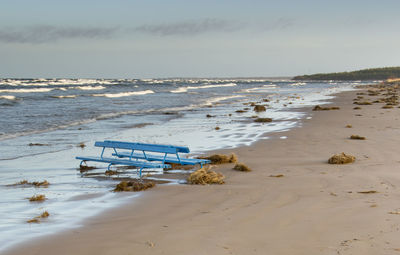 Empty blue benches on beach against wavy sea