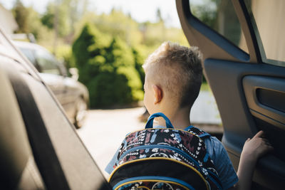 Rear view of boy with backpack opening car during sunny day