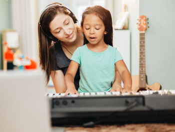 Happy mother teaching piano to daughter at home