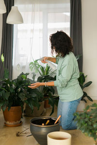 Rear view of woman holding potted plant at home