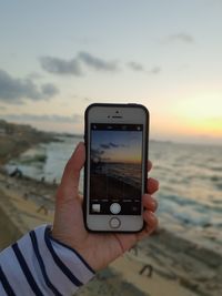 Midsection of person photographing sea against sky during sunset