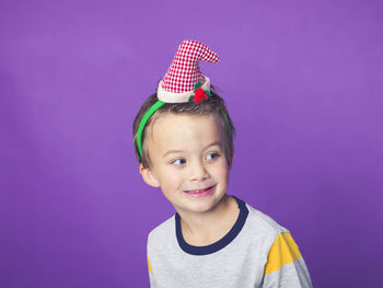 Smiling boy wearing party hat against purple background