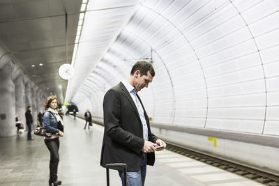 Businessman using mobile phone at railroad station