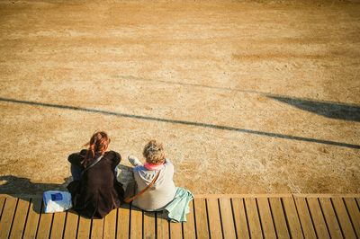 High angle view of friends sitting on boardwalk against field during sunny day