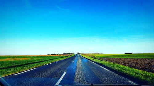 Road amidst agricultural field against clear blue sky