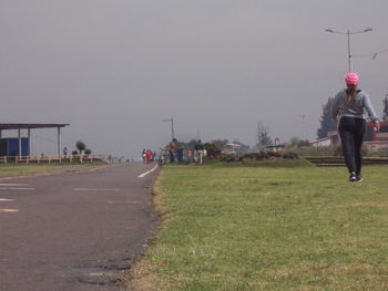 People walking on footpath in front of park against clear sky