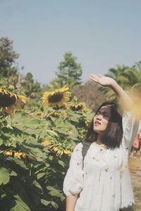 Woman standing by blooming sunflowers in sunny day