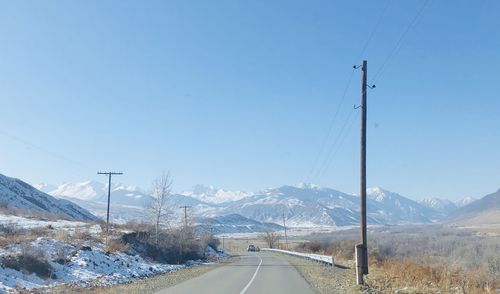 Road by snowcapped mountains against clear sky