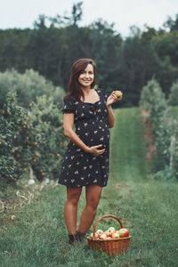 Portrait of pregnant woman holding apple standing at farm