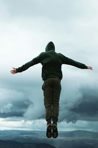 Rear view of hiker in mid-air against cloudy sky