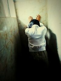 Rear view of woman standing against wall at home