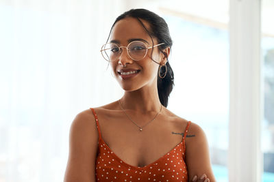 Portrait of young woman wearing sunglasses while standing against wall