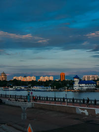 Illuminated buildings by river against sky at dusk