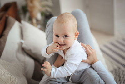 Portrait of cute baby boy sitting on bed at home