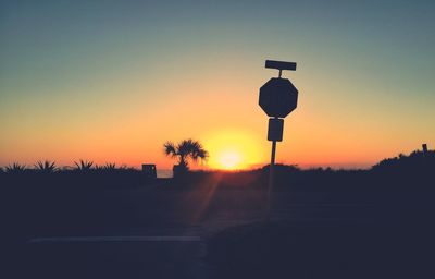 Silhouette road sign on field against clear sky during sunset