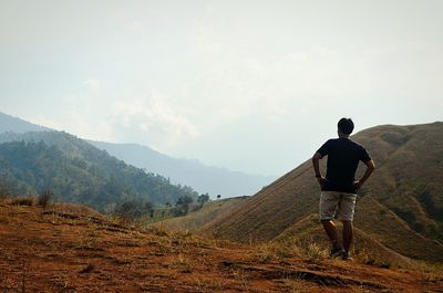 Rear view of man standing on mountain against sky