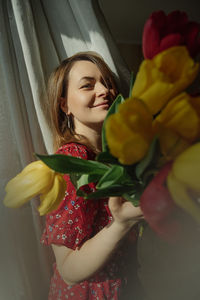 Young woman is playful natural beauty in red dress with  holding lush blooming tulips. spring mood