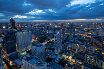 Aerial view of illuminated city buildings against cloudy sky