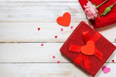 Directly above shot of red gift box with heart shape and flower on table