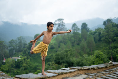 A young indian cute kid doing yoga in the mountains,wearing a dhoti