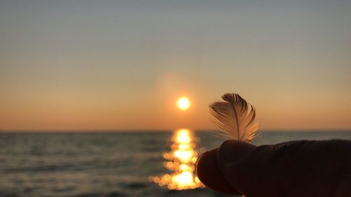 Close-up of hand holding sun at beach against sky during sunset