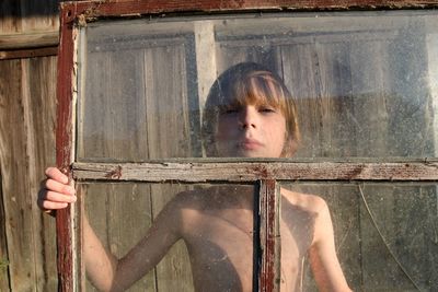 Portrait of shirtless boy looking though window