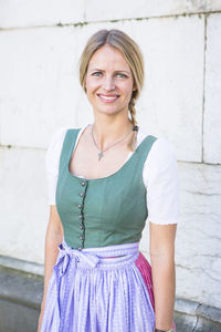 Portrait of smiling woman standing on street against wall