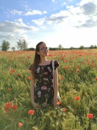 Rear view of young woman standing by poppy flowers on field