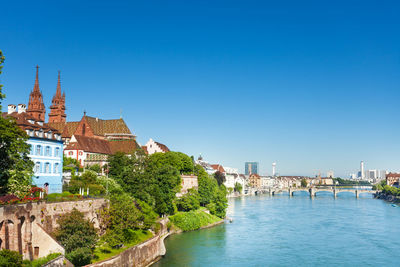 View of buildings by river against blue sky