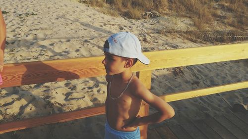 Cute shirtless boy standing on sand at beach