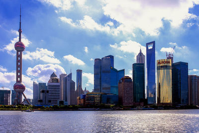 Modern buildings by huangpu river against cloudy sky