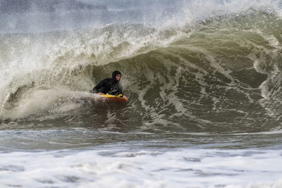 Mature male sportsperson body boarding on waves in sea at broad haven south, uk