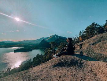 Man sitting on mountain against sky