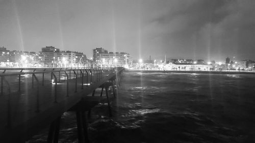 Illuminated cityscape by sea against sky at night