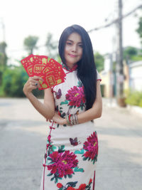 Beautiful woman holding paper with text standing on street in city