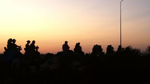 Silhouette people sitting by sea against clear sky during sunset