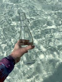 Hand holding glass bottle of crystal sea water on maldives