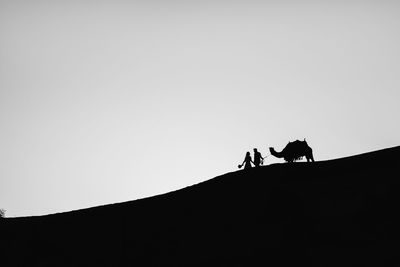 Low angle view of silhouette man riding on desert against clear sky