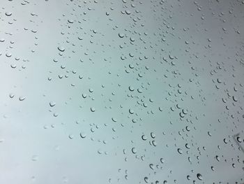 Low angle view of raindrops on window against sky